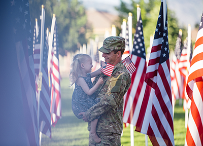 man in military uniform holding small daughter with USA flags in background