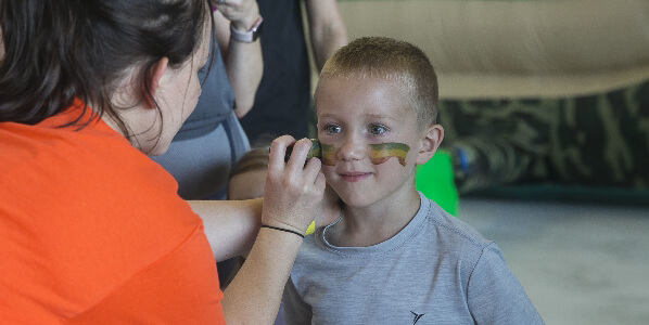 woman puts face paint on child at event support military kids