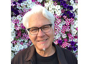 headshot of Steven standing in front of wall of flowers